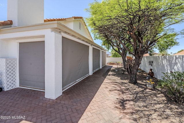 view of side of home with a tiled roof, fence private yard, a patio area, and stucco siding