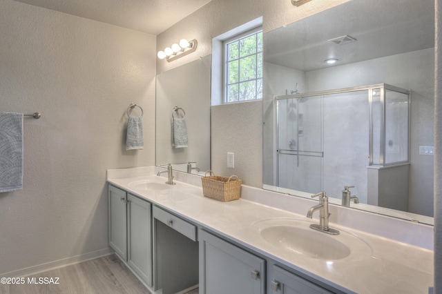 full bath featuring a sink, a textured wall, wood finished floors, and a stall shower