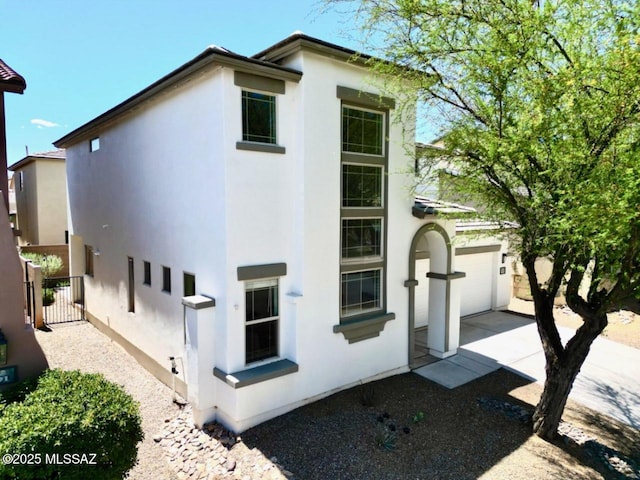 exterior space featuring a garage, stucco siding, driveway, and fence