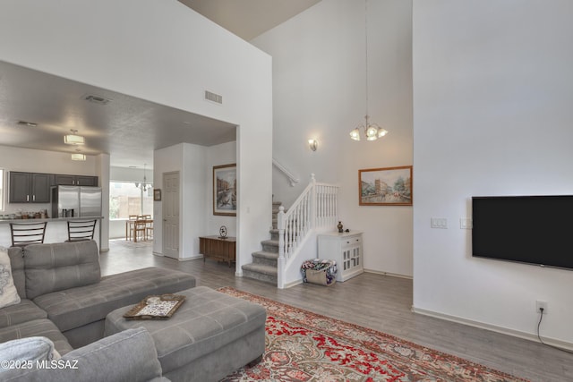 living room with a towering ceiling, visible vents, wood finished floors, baseboards, and a chandelier