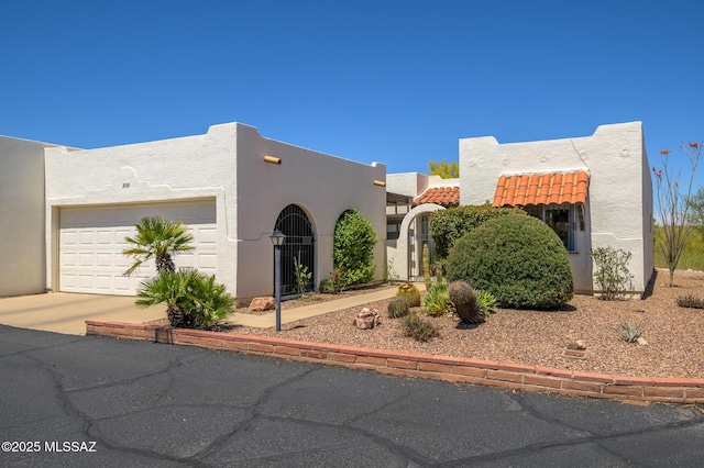 pueblo-style house with a garage, a tile roof, driveway, and stucco siding