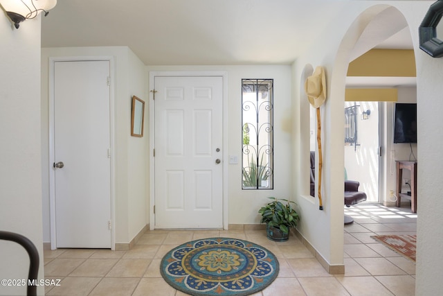entryway featuring baseboards, arched walkways, and light tile patterned flooring