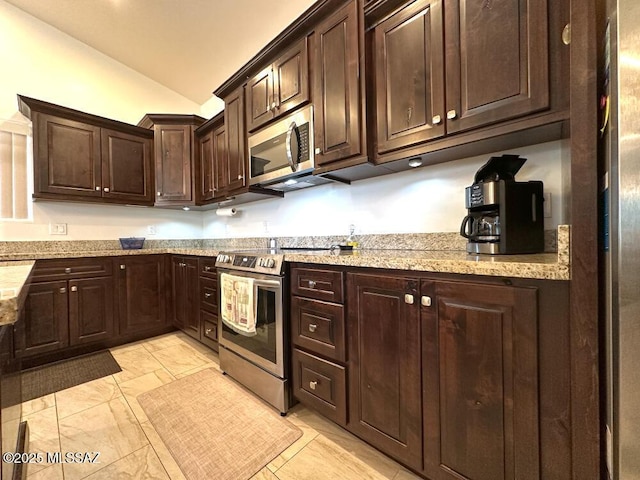 kitchen with dark brown cabinets, stainless steel appliances, vaulted ceiling, and light stone countertops