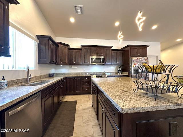 kitchen with dark brown cabinets, a sink, stainless steel appliances, visible vents, and a kitchen island