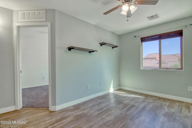 empty room with wood finished floors, visible vents, and a ceiling fan