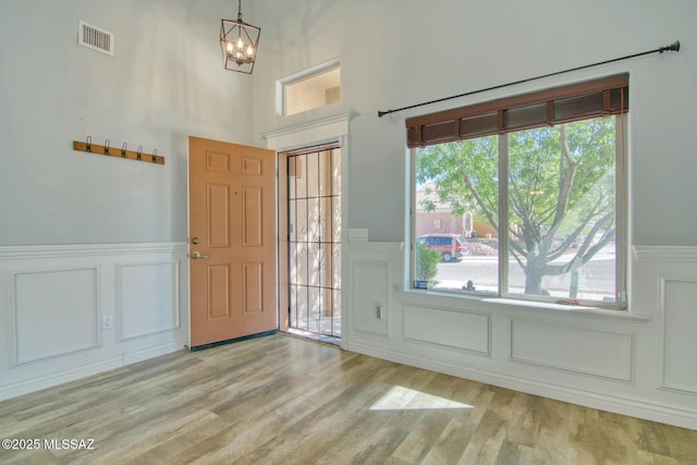 foyer featuring an inviting chandelier, visible vents, a decorative wall, wainscoting, and light wood-style flooring