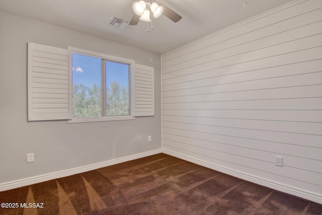 unfurnished room featuring wood walls, dark carpet, visible vents, a ceiling fan, and baseboards