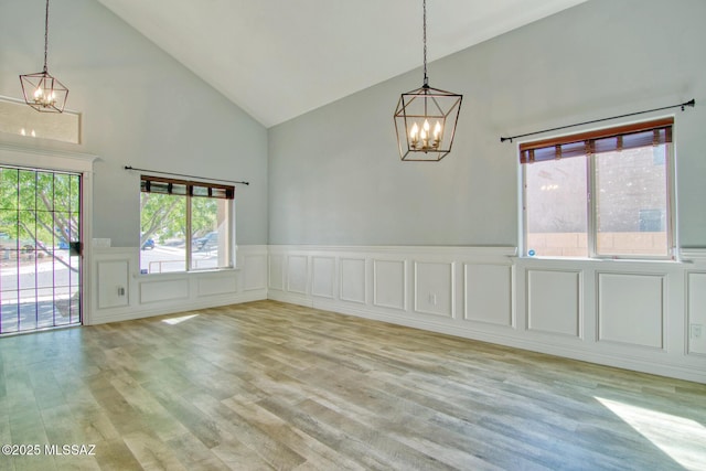 unfurnished dining area featuring light wood-style flooring, high vaulted ceiling, and a chandelier