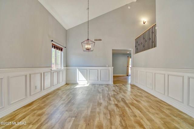 unfurnished dining area featuring visible vents, an inviting chandelier, light wood-style floors, a decorative wall, and high vaulted ceiling