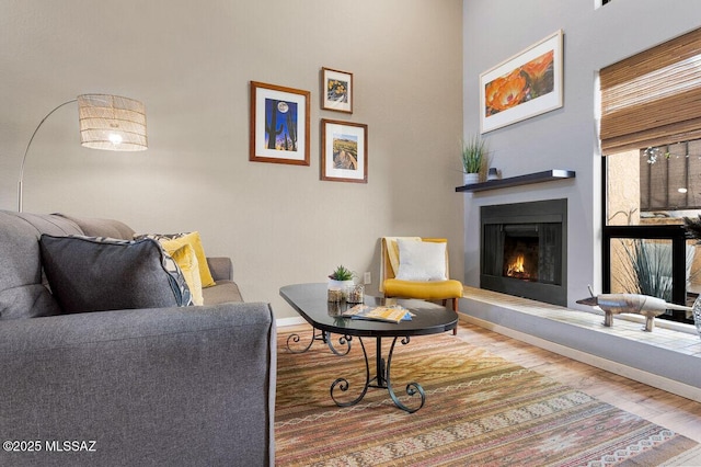 living area featuring a warm lit fireplace, wood finished floors, and baseboards