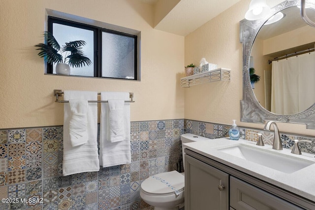 full bathroom with tile walls, a wainscoted wall, vanity, and toilet