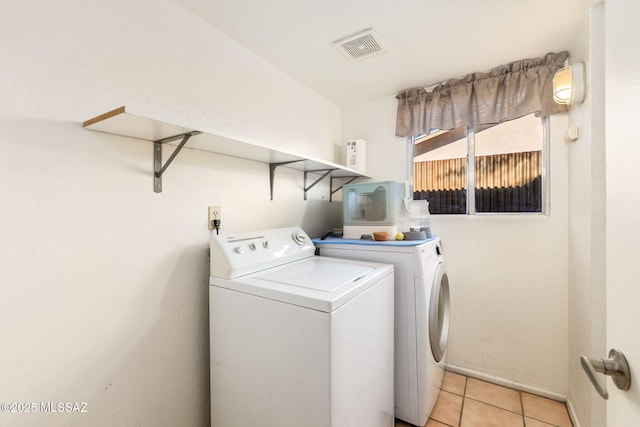 washroom featuring light tile patterned flooring, baseboards, visible vents, washer and dryer, and laundry area