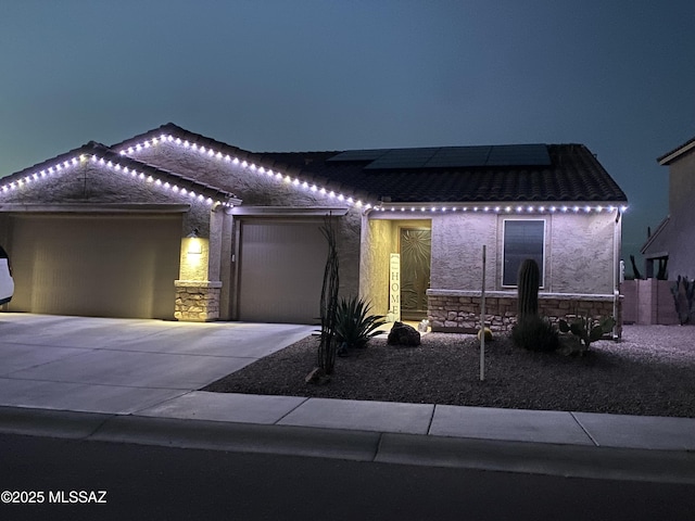 5854 W Indian Sunrise Dr, Tucson, AZ 85742 - view of front facade with a garage, stone siding, stucco siding, roof mounted solar panels, and driveway