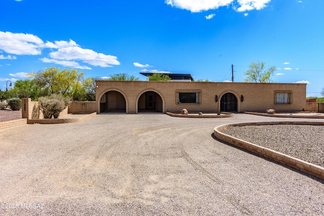 pueblo-style house with brick siding and gravel driveway