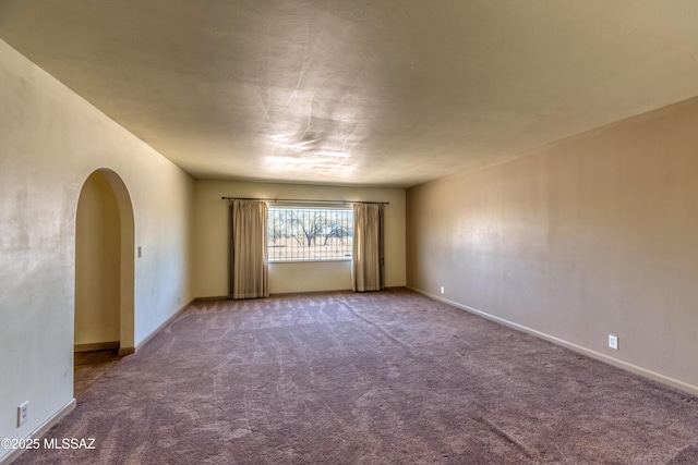 carpeted empty room with baseboards and arched walkways