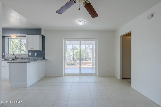kitchen with ceiling fan, backsplash, a sink, white cabinets, and dark stone countertops