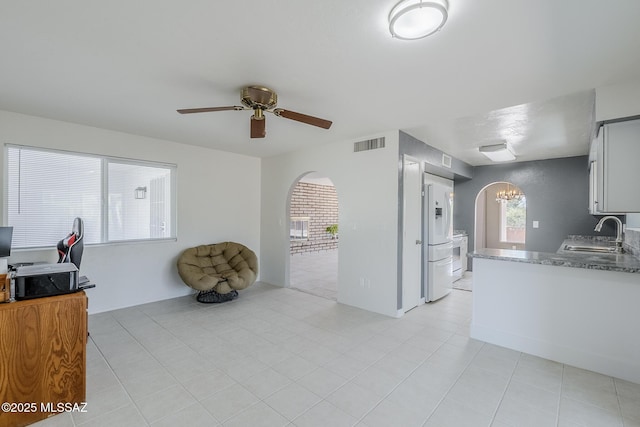 kitchen with white refrigerator with ice dispenser, a sink, arched walkways, ceiling fan with notable chandelier, and visible vents