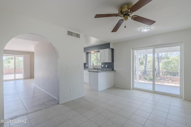 unfurnished living room with ceiling fan, visible vents, arched walkways, light tile patterned floors, and a sink