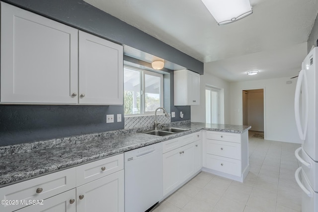 kitchen with a sink, light tile patterned floors, a peninsula, white appliances, and white cabinetry