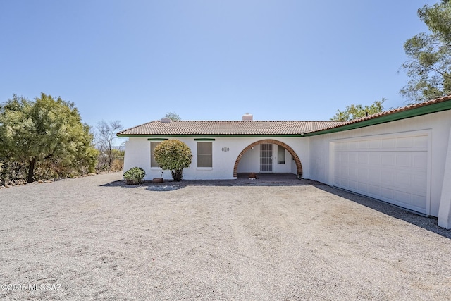 ranch-style house featuring a garage, stucco siding, a chimney, a tiled roof, and driveway