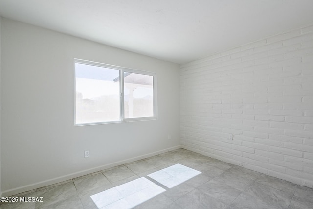 spare room featuring baseboards and brick wall