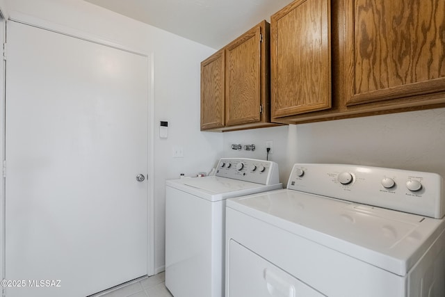 clothes washing area with washer and clothes dryer, cabinet space, and light tile patterned floors