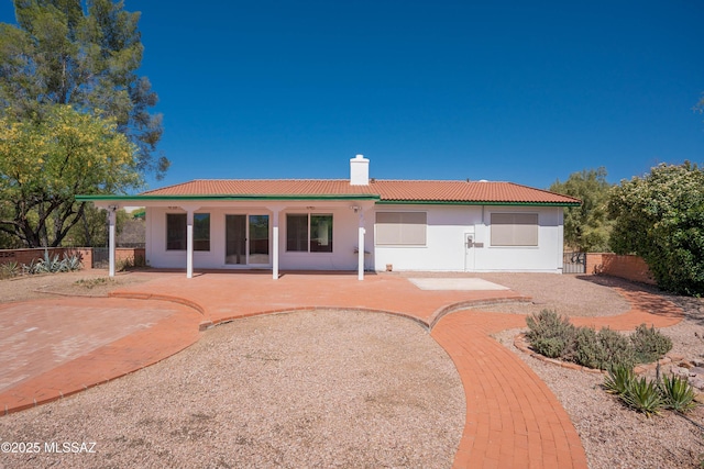 rear view of property featuring fence, a patio, stucco siding, a chimney, and a tiled roof