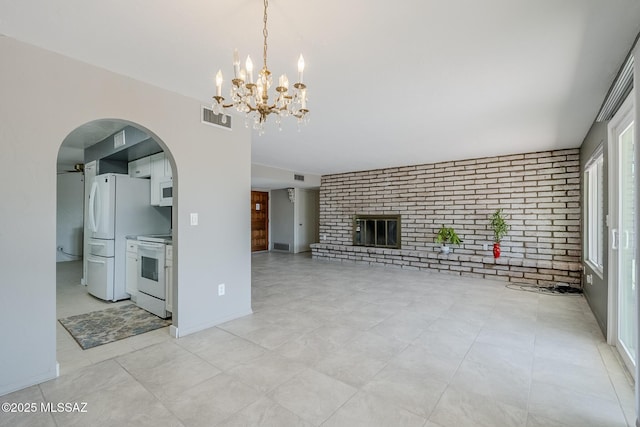 unfurnished living room with an inviting chandelier, a brick fireplace, arched walkways, brick wall, and visible vents