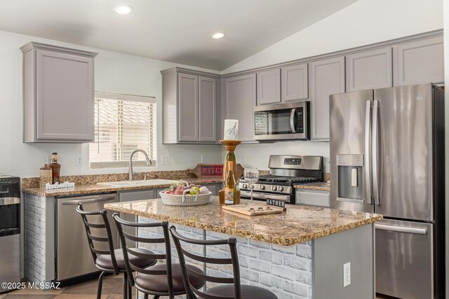 kitchen featuring light stone countertops, a kitchen island, gray cabinetry, and stainless steel appliances