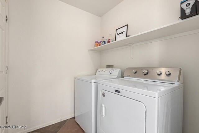 clothes washing area with dark tile patterned flooring, laundry area, washing machine and dryer, and baseboards