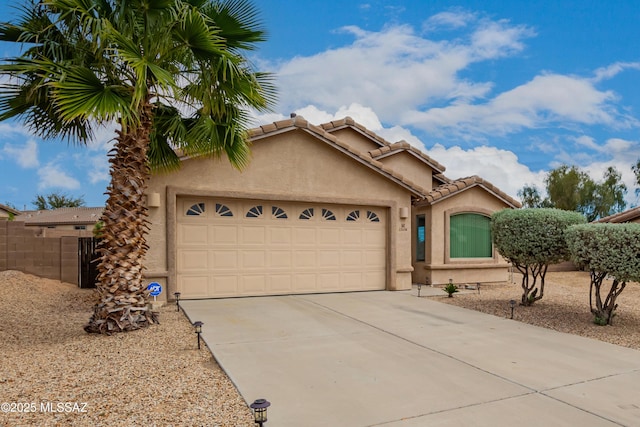 view of front facade featuring fence, a garage, stucco siding, a tiled roof, and driveway
