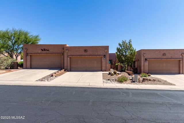 pueblo-style house with concrete driveway, a garage, and brick siding