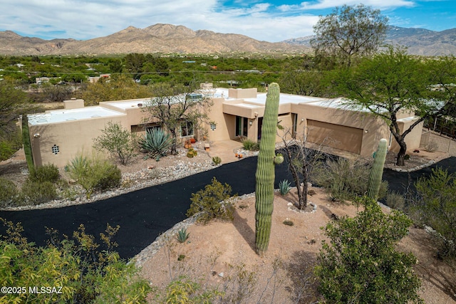 exterior space with aphalt driveway, stucco siding, a mountain view, a chimney, and an attached garage