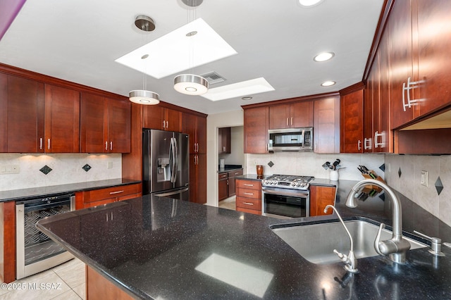 kitchen featuring beverage cooler, a skylight, hanging light fixtures, appliances with stainless steel finishes, and a sink