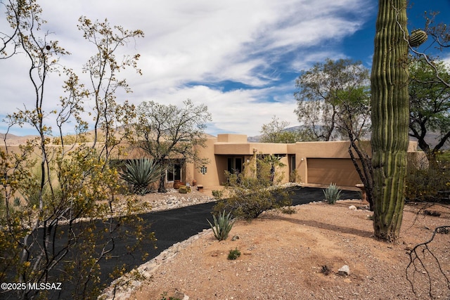 view of front facade with stucco siding, dirt driveway, and a garage
