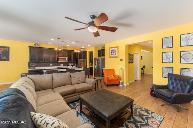 living room with a ceiling fan, baseboards, recessed lighting, and light wood-style flooring