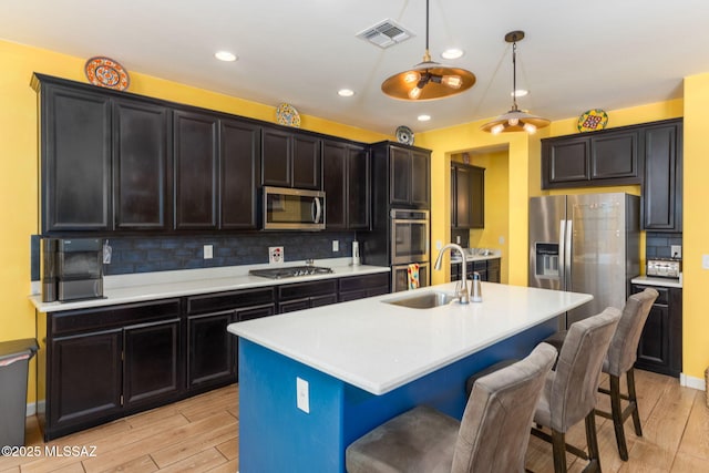 kitchen featuring stainless steel appliances, a kitchen breakfast bar, a sink, visible vents, and light wood-style floors