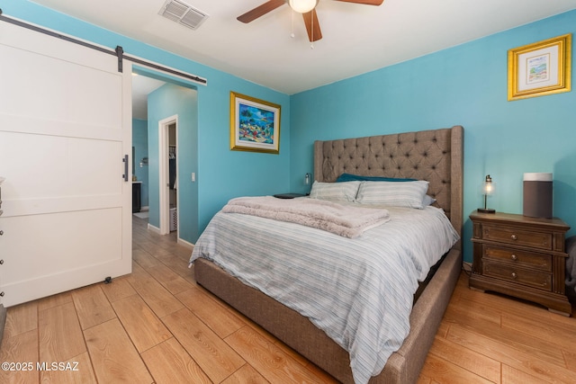 bedroom featuring a barn door, light wood-type flooring, baseboards, visible vents, and ceiling fan