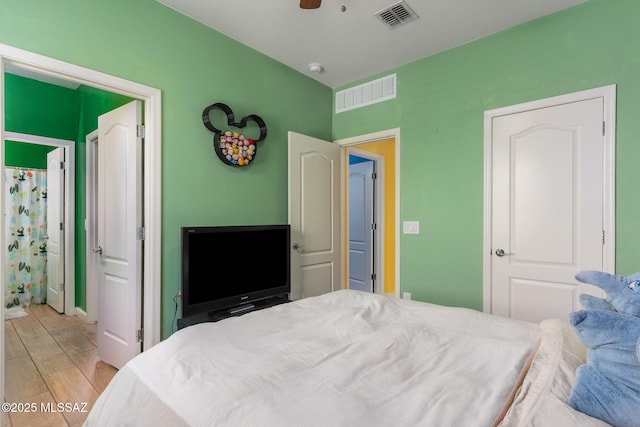 bedroom with light wood-type flooring, a ceiling fan, visible vents, and connected bathroom