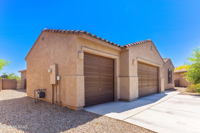 view of side of home with a tile roof, concrete driveway, fence, a garage, and stucco siding