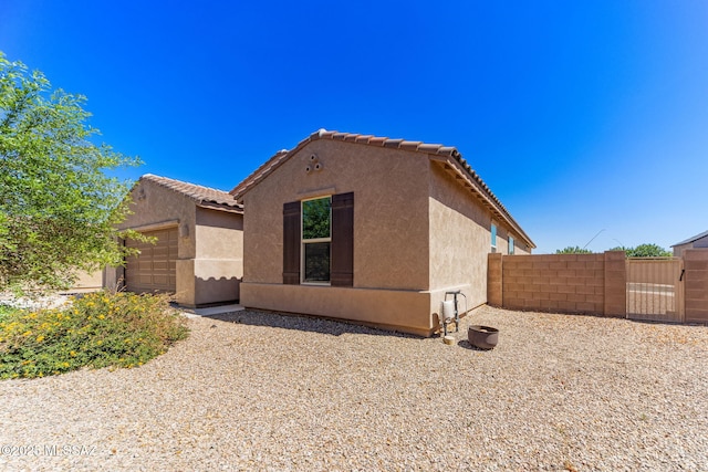 view of property exterior featuring an attached garage, a tiled roof, stucco siding, and fence