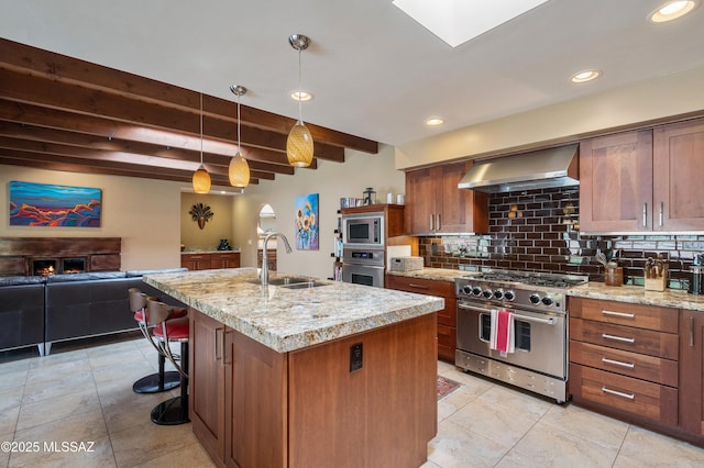 kitchen featuring wall chimney range hood, a sink, open floor plan, backsplash, and appliances with stainless steel finishes