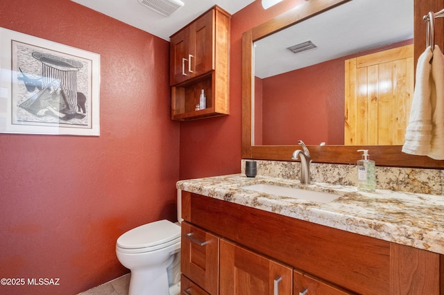 half bath with tile patterned floors, vanity, a textured wall, toilet, and visible vents