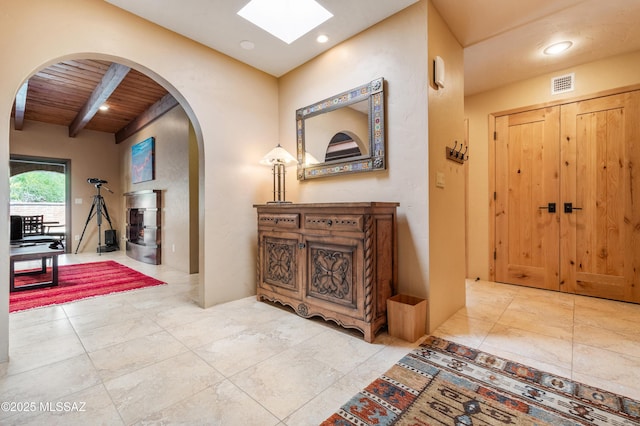 hallway with visible vents, arched walkways, beamed ceiling, a skylight, and wood ceiling