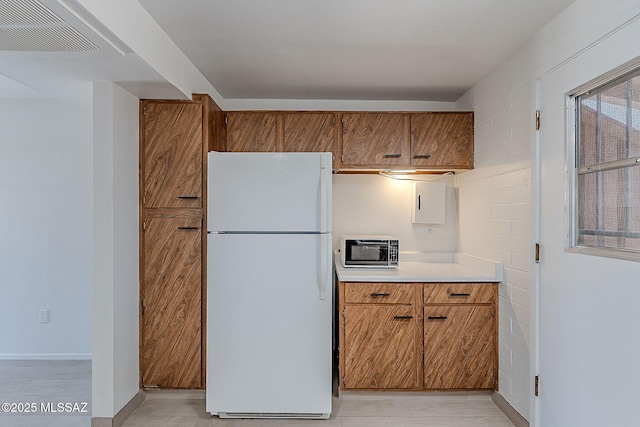 kitchen featuring visible vents, brown cabinets, light countertops, and freestanding refrigerator