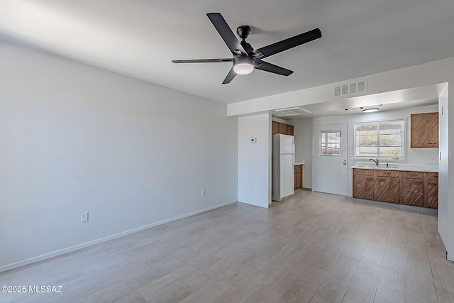 unfurnished living room featuring light wood-style flooring, a sink, baseboards, visible vents, and a ceiling fan
