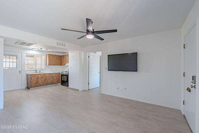 unfurnished living room featuring a sink, light wood finished floors, a ceiling fan, and visible vents