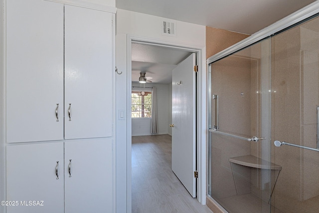 bathroom with a stall shower, a ceiling fan, visible vents, and wood finished floors