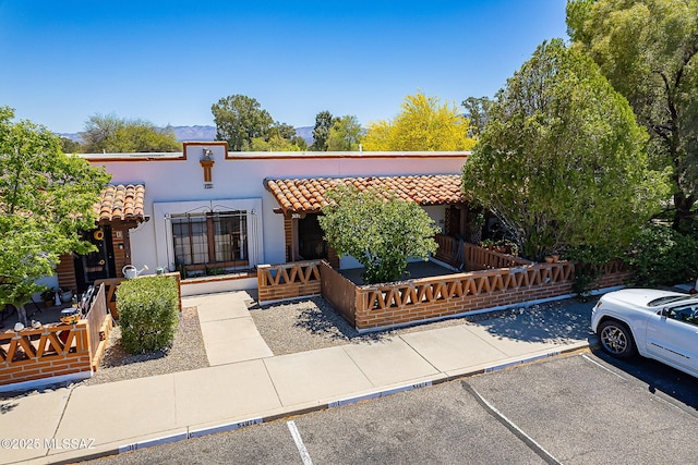 view of front facade featuring stucco siding, fence, a tiled roof, and uncovered parking