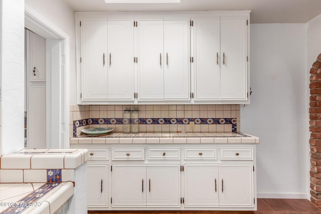 kitchen featuring tile counters, white cabinetry, decorative backsplash, baseboards, and dark tile patterned floors